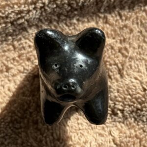 Black ceramic bear figurine on textured fabric.