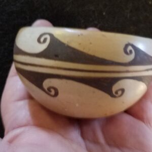 Hand holding a small, decorated clay bowl.