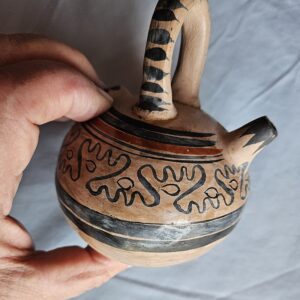 Hand holding decorative pottery with abstract patterns.
