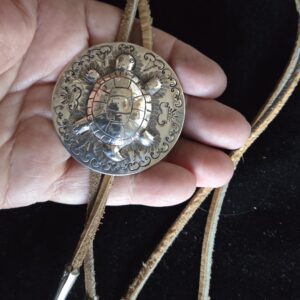 Hand holding a silver bolo tie with a detailed round clasp.